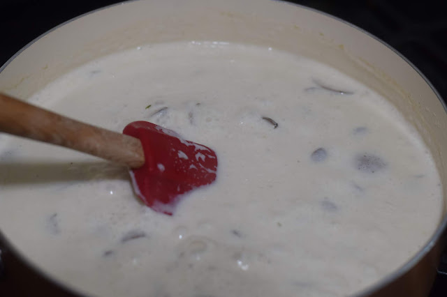 The white sauce being stirred in the pan, on the stove, with a spatula. 