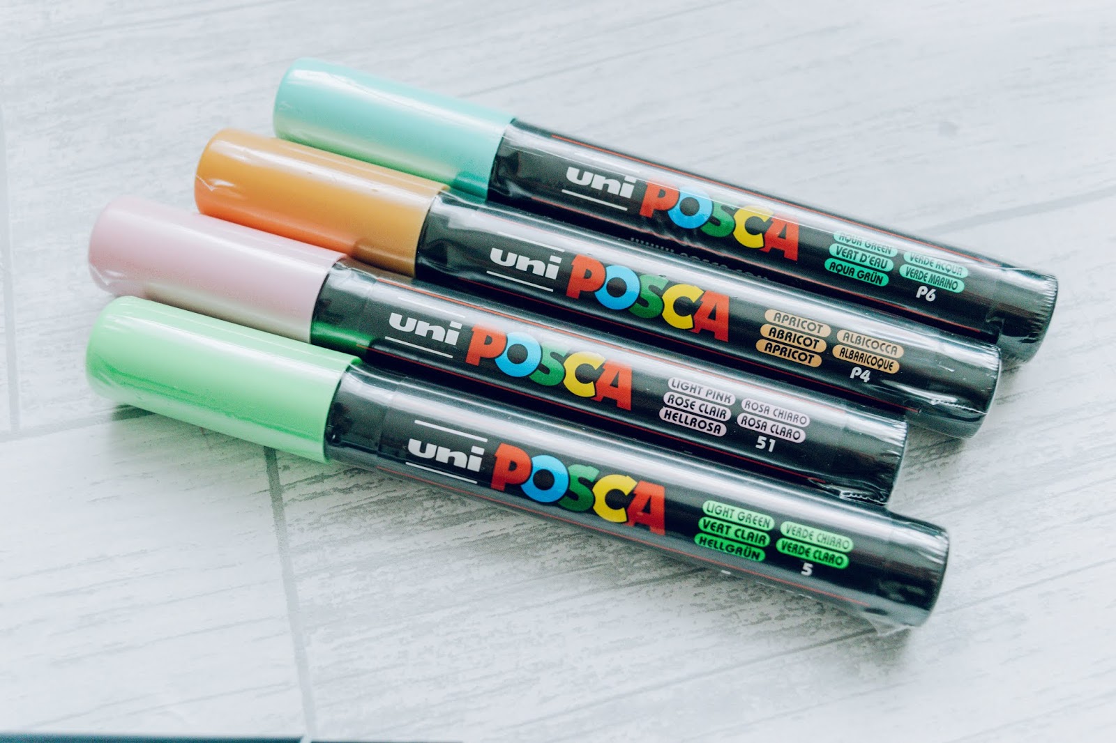 Four Posca pen paint markers in apricot, light green, light pink and aqua green.