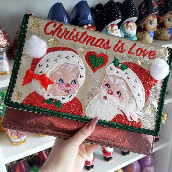 Christmas metallic clutch with Mr & Mrs Claus applique faces on front, held in hand in front of shoe shelves