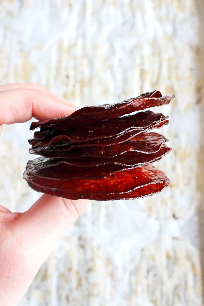 A hand holding a stack of salami chips with a white background.