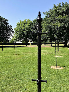 A photo of the black, iron clothes poles at the Drying Green with the trees and paths of Glasgow Green in the distance.  Photo by Kevin Nosferatu for The Skulferatu Project.
