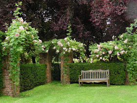 cegła w ogrodzie, drewniana ławka, róże pnące