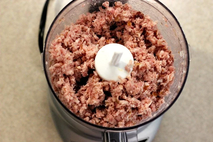 Overhead view of food processor with ham ground up for sauerkraut ball recipe