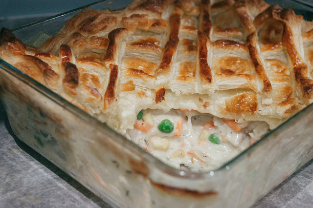 A chicken and vegetable pie in a glass oven dish with a portion taken out