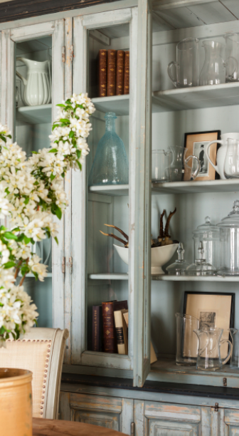 Detail of a weathered painted dining room hutch with glass doors. Come see this Rustic Elegant French Gustavian Cottage by Decor de Provence in Utah! #frenchcountry #frenchfarmhouse #interiordesigninspiration #rusticdecor #europeanfarmhouse #housetour