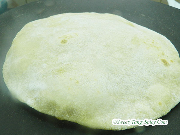 Hands flipping chapatis on a hot tawa, while gently pressing the bubbles to encourage puffing.