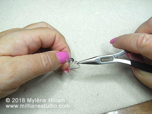 Attaching the clasp to each end of the chain with jump rings using chain nose pliers.