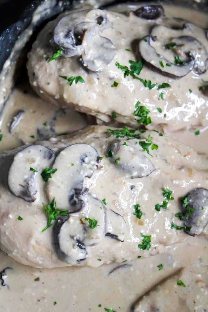 Closeup top view of chicken with mushroom cream sauce in a black crock pot.