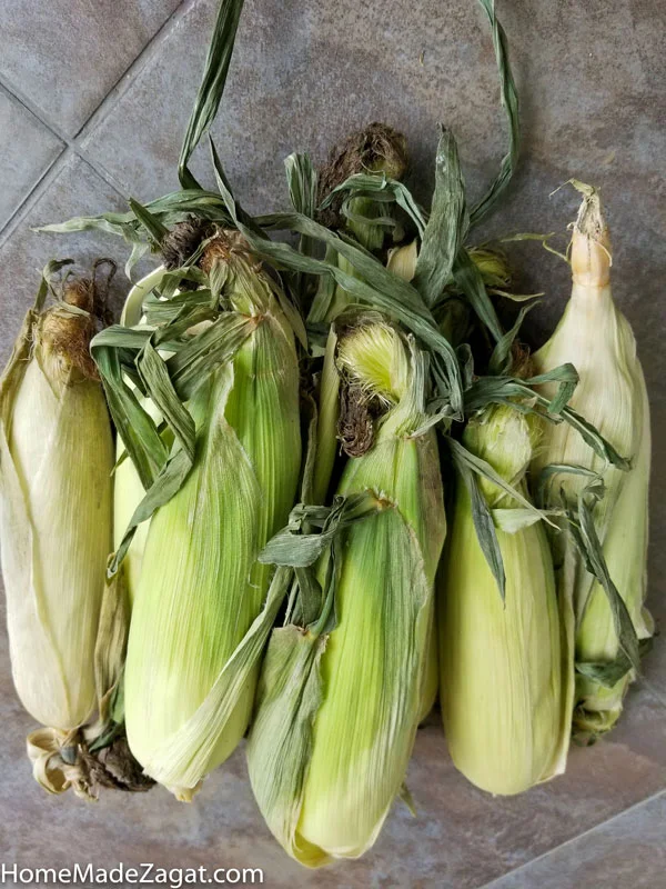 a bussel of corn on the cob in husk.