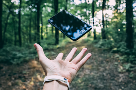 a mobile phone being thrown into the air in the middle of a forest