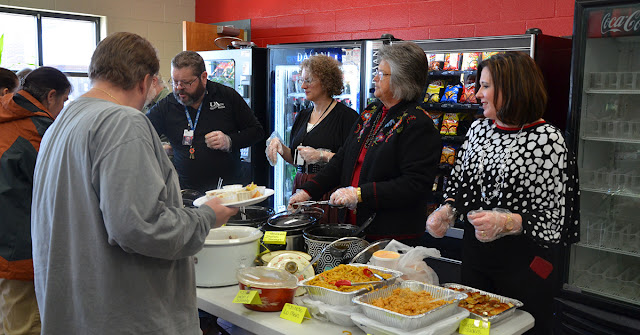 men and women stand around plates of food