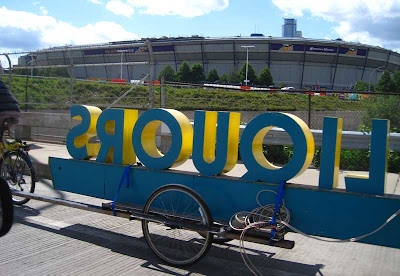 Bicycle trailer with 3D sign reading LIQUORS backwards, with the Minneapolis Metrodome in the background