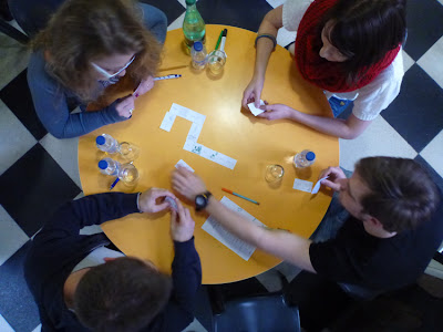 Vogelperspektive: Gelber Tisch und junge Leute, die Domino spielen, die Dritte