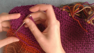 the wrong-side of a garter stitch scarf.  Someone is using a tapestry needle to weave in ends behind the existing stitches.
