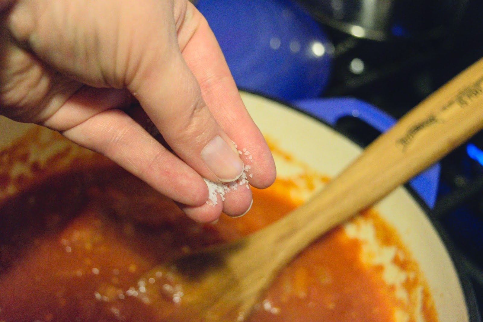 Salt being added to the marinara in the pot.  