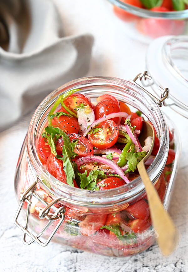 a jar with marinated cherry tomatoes with chopped basil and cilantro