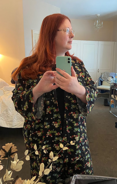 A red-haired woman in a black floral trouser suit.