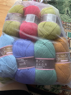 7 100g skeins of various colors of yarn: dark moss green, bright dark pink, moss green, light blue, blue-purple, and rust.