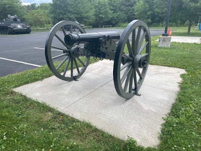 Civil War era cannon on carriage with two large wheels sits on a concrete pad in the middle of a grassy parking lot median