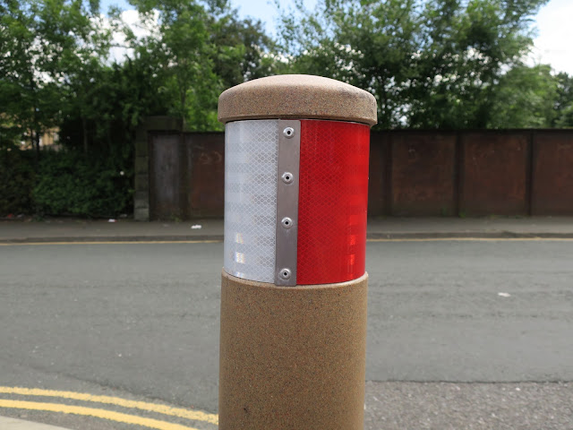 Brown, red and white bollard in front of rusty bridge by road with yellow markings.