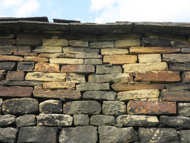 Clean stones mixed with old stones where wall of old, slate roofed outbuilding has been mended.