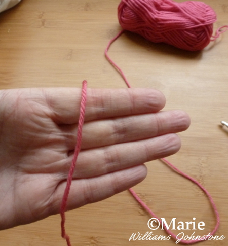 Drape the end of the red pink crochet yarn over the fingers on your hand