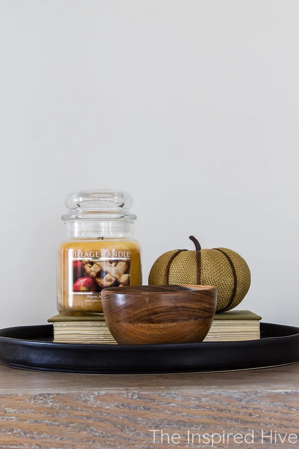 Simple fall vignette with book, candle, pumpkin, and wooden bowl on black ceramic tray
