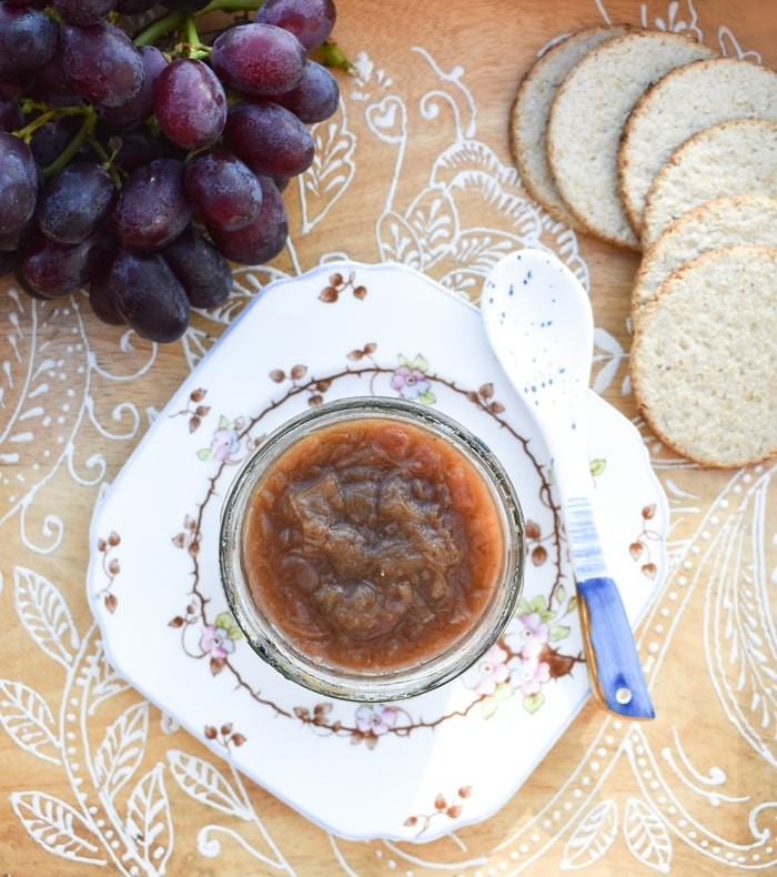 Rhubarb chutney in a jar on a wooden tray with grapes and oatcakes