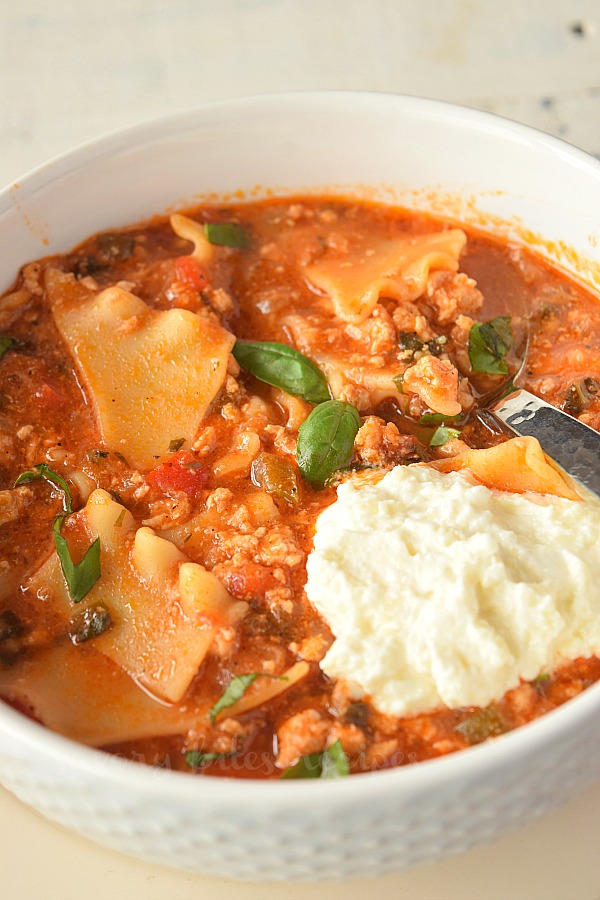 close look at a white bowl with chicken lasagna soup topped with ricotta