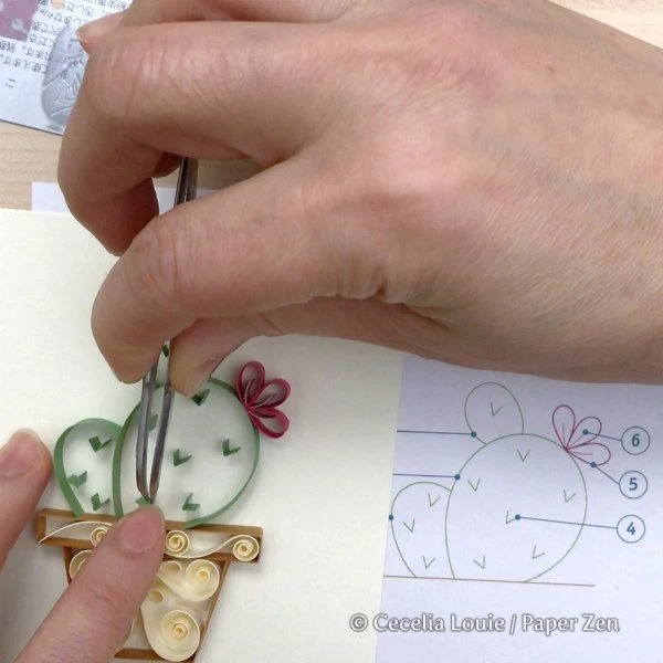 hand showing placement of on-edge folded paper strip on quilled cactus card
