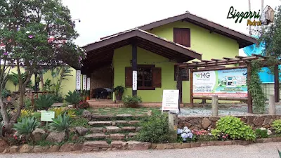 Piso com tijolo de demolição no terraço com os pilares de dormente na construção da cabana rústica com a escada de pedra, piso de pedra com junta de grama e no fundo a parede de pedra no terraço da cabana.