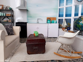 1/12 scale modern miniature scene of a kitchen and lounge in shades of white, teal, grey and light wood in a flat overlooking the sea.