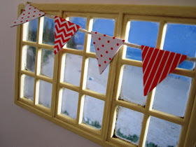 Modern one-twelfth scale miniature window overlooking the beach, with red and white bunting strung across it.