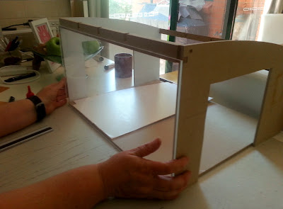 Holding a piece of cut perspex up against the front of a doll's house kit.