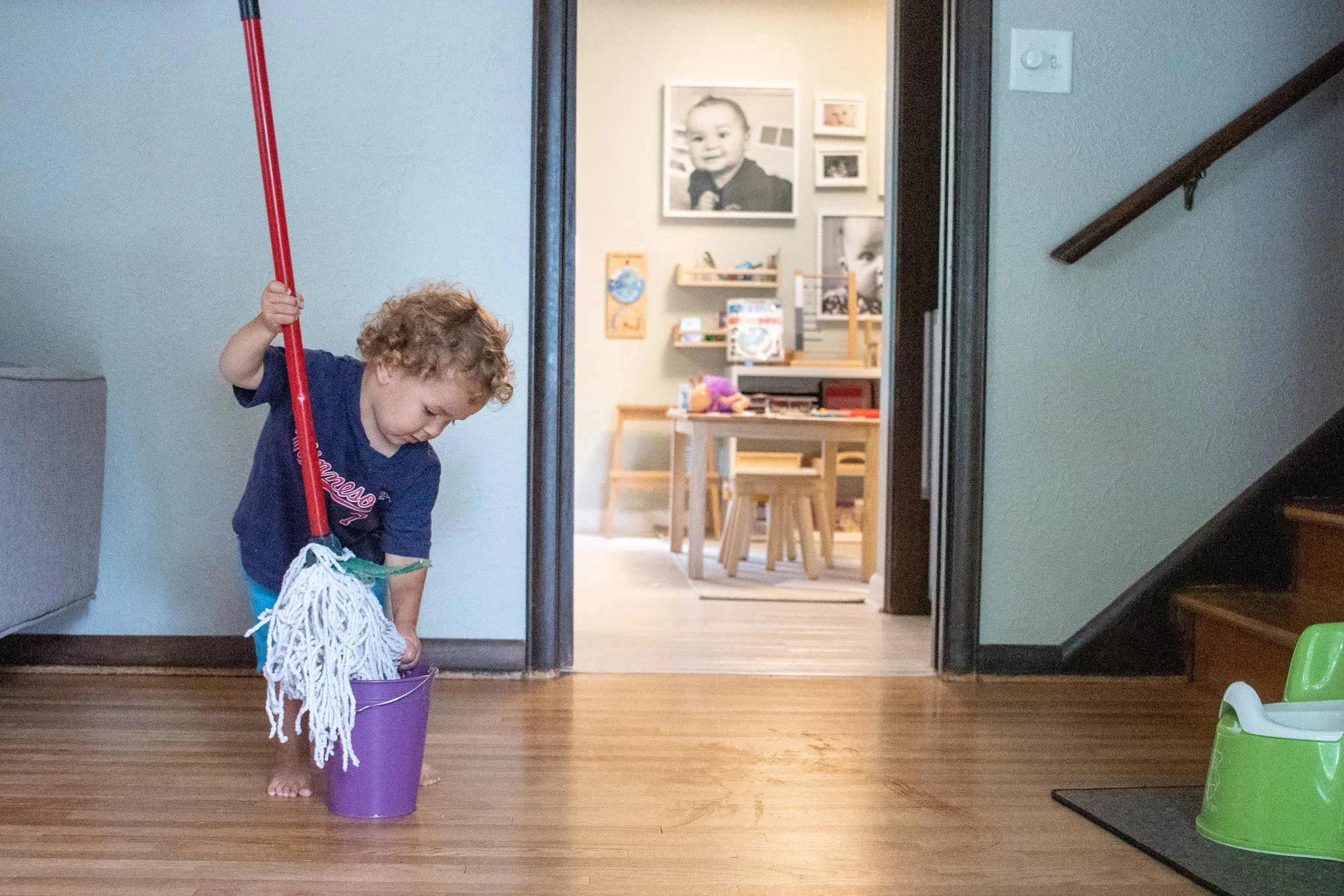 Montessori toddler places small child sized mop into bucket of water to wash floors.