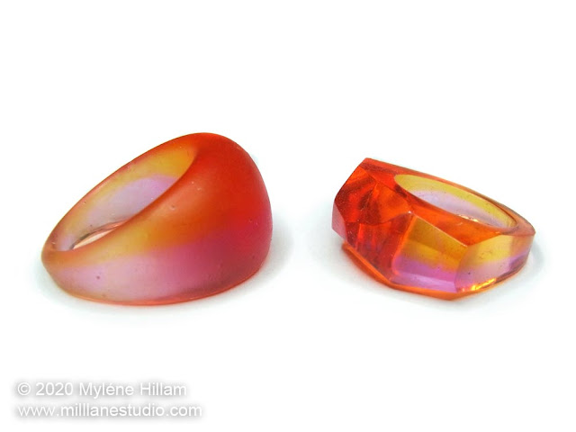 A pink an orange domed ring with a matte surface and a pink and orange ring with a faceted glossy surface