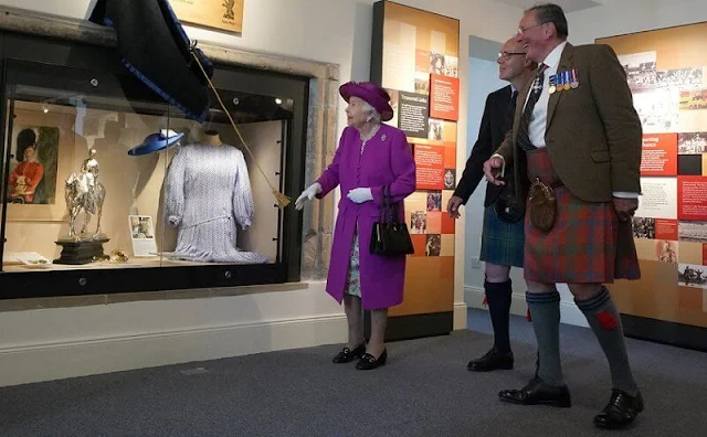 The Queen wore a floral print dress and purple coat and purple hat. diamond brooch