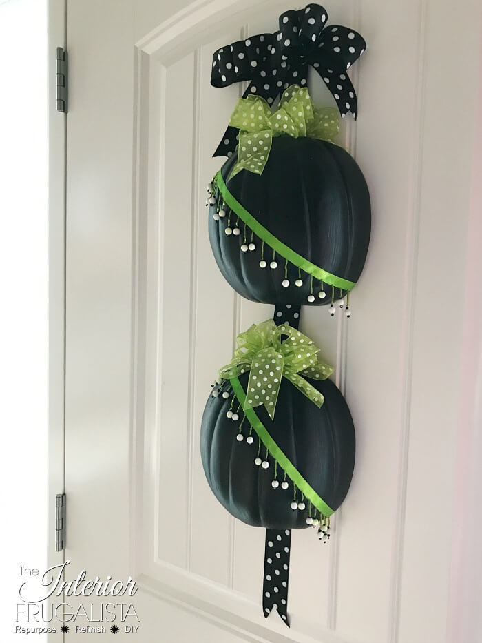 An easy peasy Halloween half pumpkin door hanger that won't scare trick or treaters made with craft pumpkins and assorted green and black ribbon.
