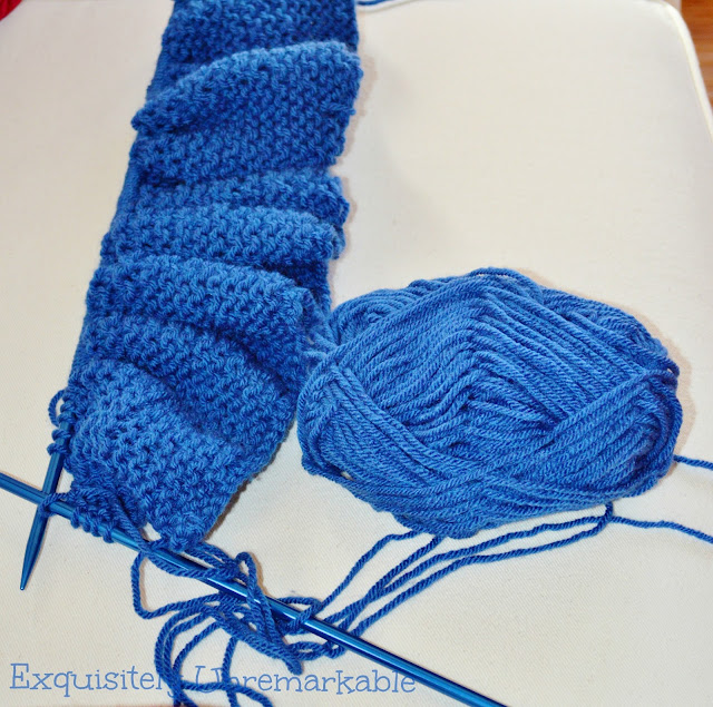 Blue garter stitch scarf in process with needles and a ball of yarn