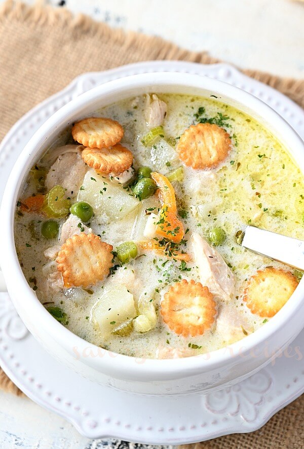 a close up of a white bowl with homemade chicken pot pie soup topped with oyster crackers