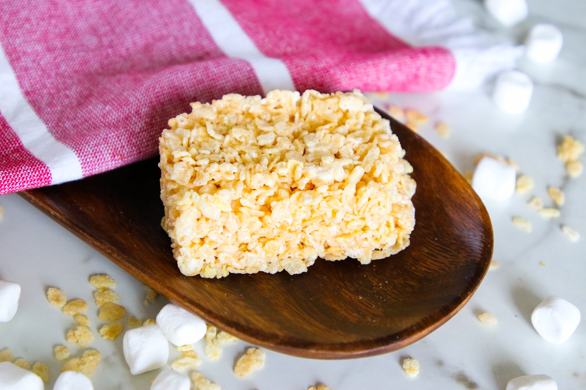 Single serve rice krispie treat Rice krispie treat on a wood platter with a red dish towel with rice krispies and marshmallows scattered on the table