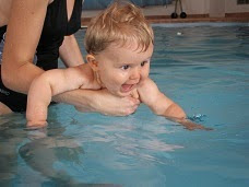 Picture of a baby being held as they paddle in the water. Do You fall for any of the eight most common mistakes singing swim teachers make.