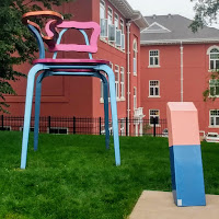 Aluminum sculpture of a school desk and eraser in front of a brick building