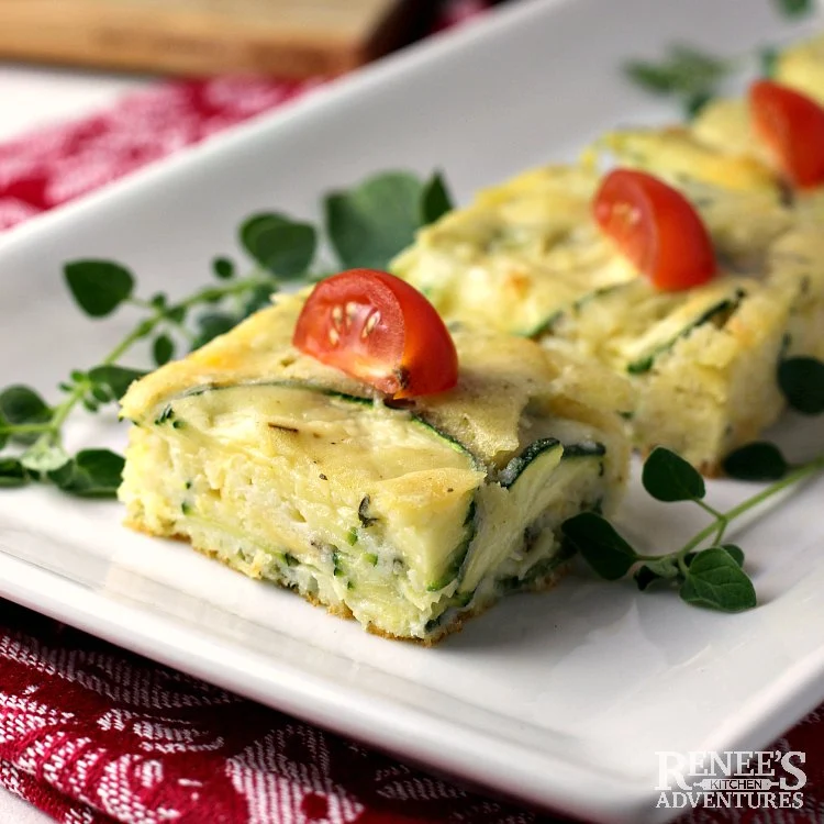 Zucchini Appetizer on a white serving plate garnished with fresh oregano and cherry tomatoes.