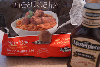 A bag of froze meatballs along side a bottle of BBQ sauce.