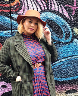 Plus size woman with blonde hair wearing hat, tweed coat and print dress