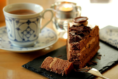 Ein Stück Schoko-Torte mit einer Gabel, links davon steht eine altmodische Tasse mit Kaffee
