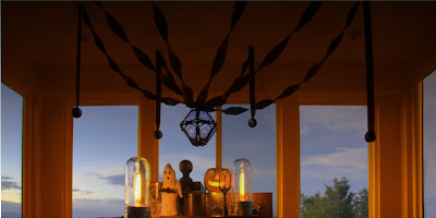 Sunset photo of A vintage-style table setting of black crepe paper with a Bindlegrim lantern, also with refurbished lighting, wooden boxes, vintage pumpkin, and paper mache ghost by Hobgoblin