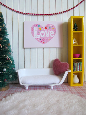 Modern miniature dolls house scene with a Christmas tree, bathtub sofa and a 'love' picture on the wall and matching heart-shaped cushion on the sofa.