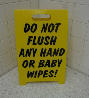 Yellow floor A-frame sign, like one used for wet floor notices, that says DO  NOT FLUSH ANY HAND OR BABY WIPES